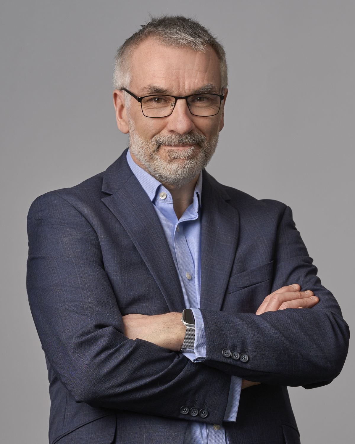 Corporate headshot of a senior director in a navy suit, photographed on a grey studio backdrop in Manchester