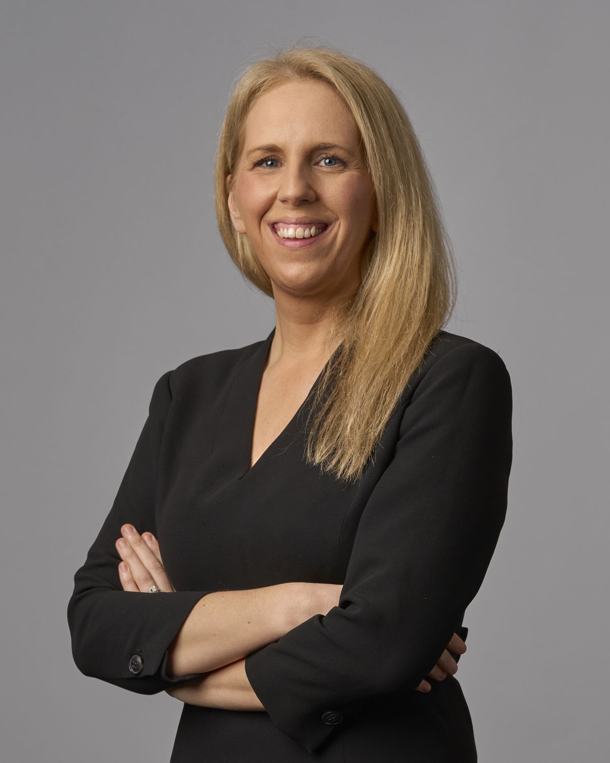 Corporate headshot of a smiling professional woman in a black dress with arms folded