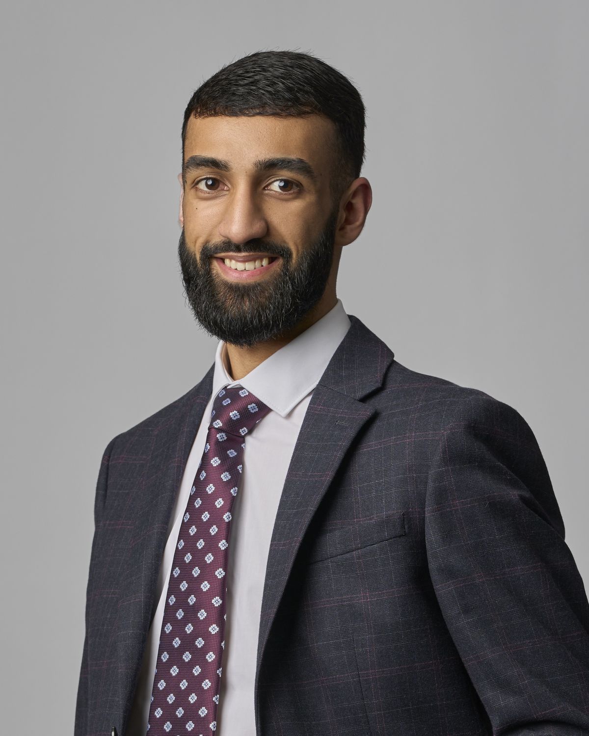 Corporate headshot of a young professional man in a checked suit and tie