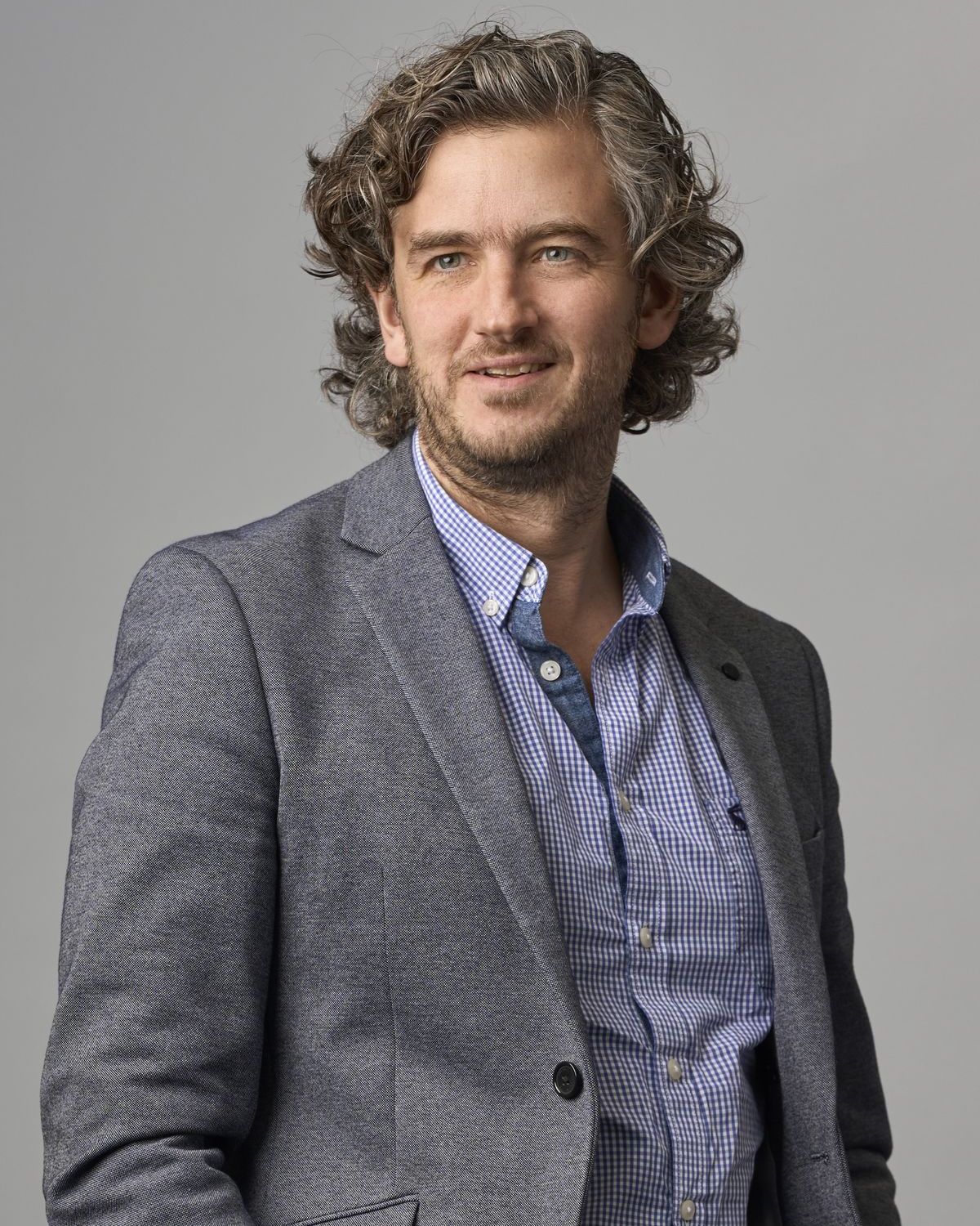Corporate headshot of a professional man with curly hair in a grey blazer