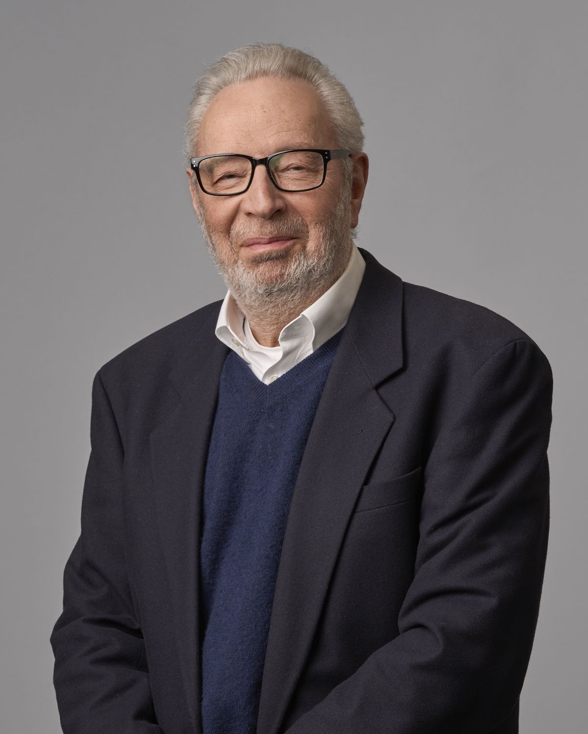 Corporate headshot of a senior professional man in glasses and a dark blazer